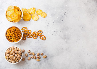 Fototapeta na wymiar Pretzel and potato crisps and pistachio in white ceramic bowl on stone kitchen table background. Space for text. Snack for beer