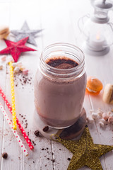 Cocoa with marshmallow and straws in the glass jar decorated with christmas stars on the wooden white table for the winter holidays