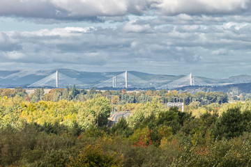 A photograph of the new Queensferry bridge over the Firth of Forth near Edinburgh, Scotland, UK, also showing the county of Fife and a forest changing colour in the fall. 