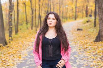 Portrait of a beautiful and dreamy young woman with long wavy hair in autumn park