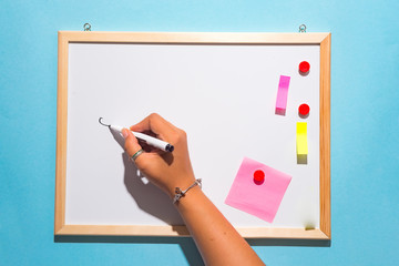 The hand of a woman holding a marker ready to write something on a white board on blue background,...