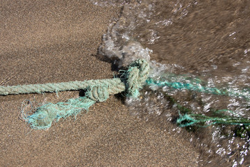 Close up of rope knot on sand beach. A gentle wave is comming. Safety concept coast.