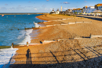 late afternoon autumn sunshine turns the pebbles on the beach and wooden groyne water breakers in...