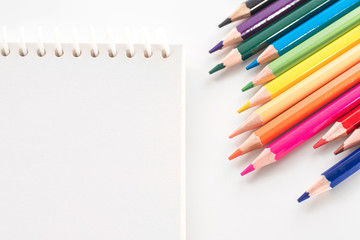 notepad with color pencil on white table view from above