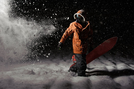Professional snowboarder in orange sportswear with a board at night