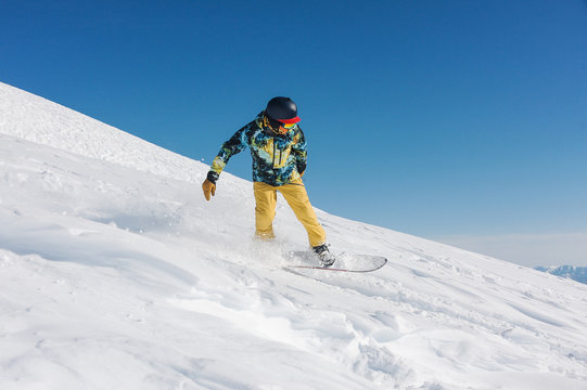 Young snowboarder in stylish sportswear riding down the slope in Georgia, Gudauri