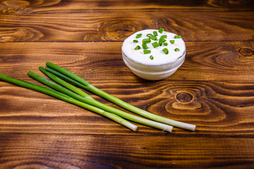 Obraz na płótnie Canvas Glass bowl with sour cream and green onion on wooden table