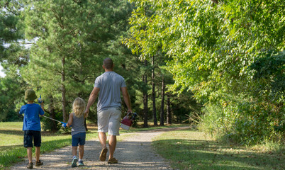 Fototapeta premium Dad, daughter, and son walking on path with fishing gear