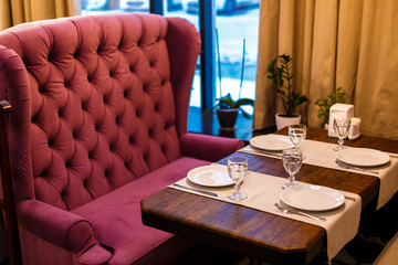 A table by the window in a cafe, a table setting - a vintage burgundy sofa, a wooden table of brown color