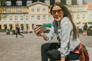 Young beautiful woman sitting in the city center taking a self portrait with her phone.