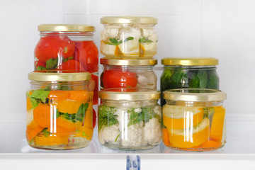 Fototapeta na wymiar Variety glass jars homemade pickled vegetables stand in fridge. Fermented healthy natural vegetarian food concept.