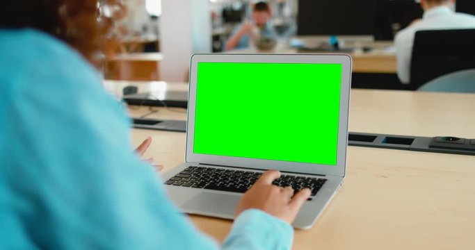 Young black African American woman sitting in the office, working on a laptop, green screen chroma key. 4K UHD 60 FPS SLO MO