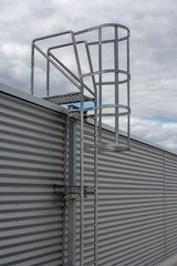 Steel ladder with protection, attached to an industrial, production hall or building. Safety ladder for roof maintenance or fire emergency escape ladder on a building in vertical angle.
