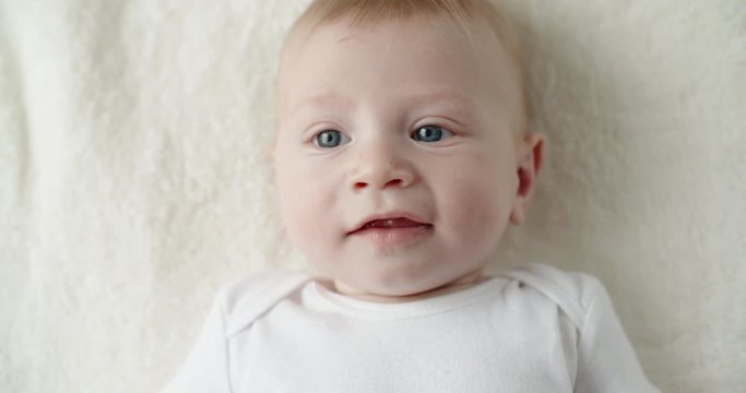 Cute caucasian baby lying on white bed sheet, happily smiling and laughing. happy childhood concept closeup 4k