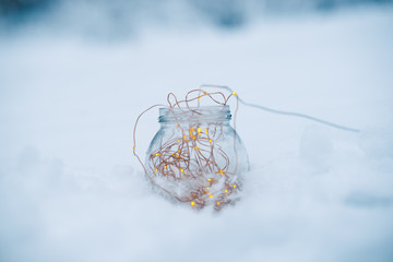 Glass jar with garlands in the snow