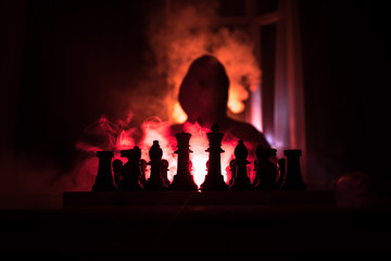 Man playing chess. Scary blurred silhouette of a person at the chessboard with chess figures. Dark toned foggy background.
