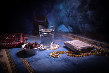Water and dates. Iftar is the evening meal. View of decoration Ramadan Kareem holiday on carpet. Festive greeting card, invitation for Muslim holy month Ramadan Kareem. Dark background