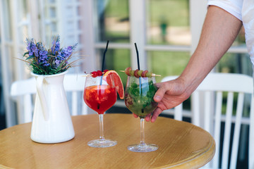 A man and a woman ordered tasty cocktails at the bar, the waiter left them at their table, the man takes a glass, wants to try a drink. Cropped frame of a male hand with a glass.