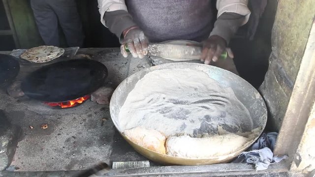 Man rolling dough of paratha on rolling board and frying it on frying pan