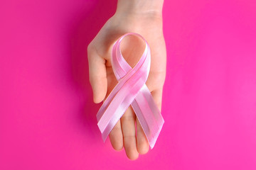 Obraz na płótnie Canvas Woman hands holding pink colored ribbon - international symbol of breast cancer awareness and moral support for illness survivors. Isolated background, copy space, close up, top view fat lay.