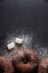 Top view of chocolate glazed doughnuts with powdered sugar and sugar cubes on a textured surface 