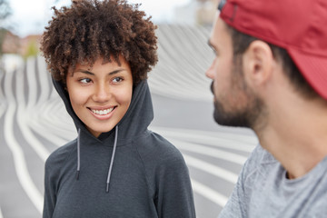 Photo of cheerful teenagers in fashionable clothes, being in high spirit, have pleasant unforgettable time together, pose outdoor, going to play basketball. Friendship concept. Recreation and mood