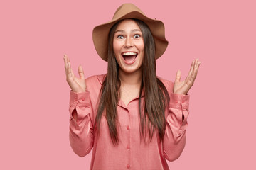 Waist up shot of overjoyed European woman gestures actively, exclaims with happiness, cant believe in success and triumph, wears fashionable clothes, isolated on pink background. Positiveness concept