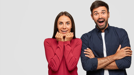 Amazed girlfriend and boyfriend stare at camera, notice something unbelievable, stare at camera, stand closely to each other, isolated over white background with copy space for your advertisement