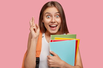 Photo of cheerful brunette woman with overjoyed look keeps fingers crossed, believes in everything...