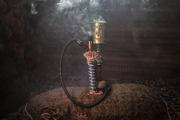 Hookah hot coals on shisha bowl making clouds of steam at Arabian interior. Oriental ornament on...