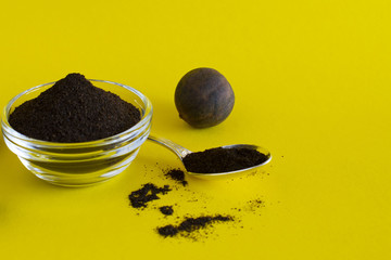 Black lemon powder in a glass bowl and a silver spoon on the yellow background. Copy space.
