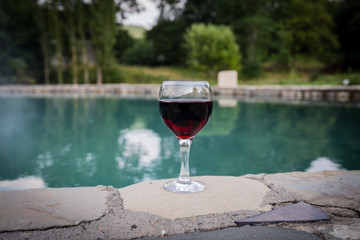 Drink in tall glass in poolside. Refreshment on summer day. Purple juice cocktail or vine. Mountain forest background.
