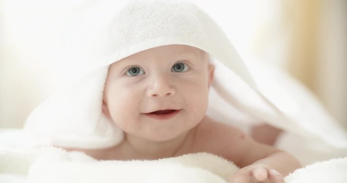 Cute caucasian baby lying on white bed sheet, happily smiling and laughing. happy childhood concept closeup 4k