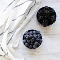 Full blue bowls of berries on a white wooden background, overhead view. From above, top view, flat lay.