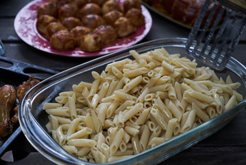 Party snack food table with baked potatoes, fried chicken drumsticks, italian pasta and puff pastry buns bread, close-up. Table with variety food top view. 