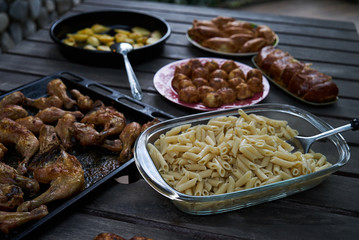 Party snack food table with baked potatoes, fried chicken drumsticks, italian pasta and puff pastry buns bread, close-up. Table with variety food top view. 