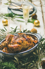 Christmas or New Year celebration table setting. Roast chicken, plates, silverware, glass and toy holiday decoration over rustic white wooden background, selective focus