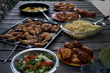 Party snack food table with baked potatoes, fried chicken drumsticks, italian pasta and puff pastry buns bread, close-up. Table with variety food top view. 
