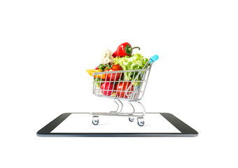 A shopping cart with fresh vegetables close-up stands on a smartphone tablet isolated on a white background. Online Shopping
