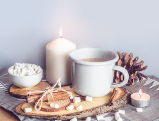 Obraz na płótnie Canvas A cup of hot cocoa with marshmallows and candles on a table surrounded by winter or Christmas decor, closeup