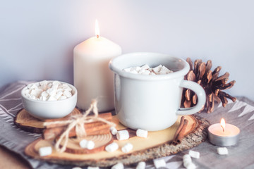 Obraz na płótnie Canvas A cup of hot cocoa with marshmallows and candles on a table surrounded by winter or Christmas decor, closeup