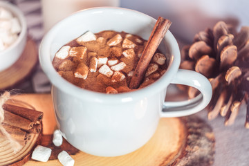 A cup of hot cocoa with marshmallows and candles on a table surrounded by winter or Christmas decor, closeup
