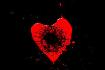Red heart symbol broken into small splinters of glass from a shot from a pistol with a hole from a bullet isolated on a black background. Allegory of the unhappy love of a broken heart.