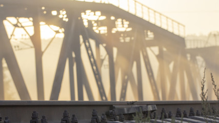 A railway bridge in the morning fog or smoke through which the rays of the sun shine