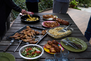 Catering buffet food table with baked potatoes, fried chicken legs, pasta and vegetable salad. People at a party taking different food, outdoor. Colleagues Buffet Party Brunch Dining Concept
