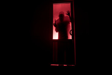 Silhouette of an unknown shadow figure on a door through a closed glass door. The silhouette of a human in front of a window at night. Scary scene halloween concept
