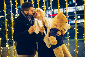 Beautiful young couple in love enjoying Christmas or New Year night on a city street.