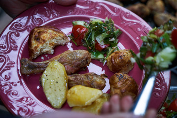 People at a party taking different food, outdoor. Catering buffet food table with baked potatoes, fried chicken legs, pasta and vegetable salad