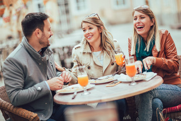 Group of three friends using phone in outdoor cafe on sunny day, eating pizza