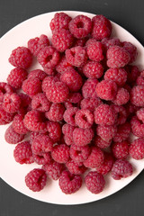 Raspberry on a pink plate on black background, overhead view. Flat lay, top view, from above. Close-up.